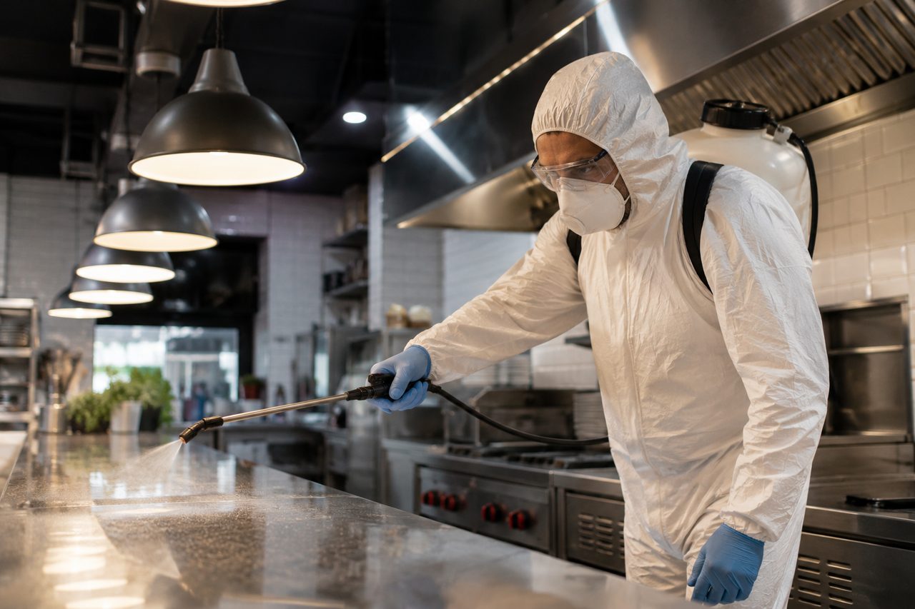Personal con equipo de protección desinfectando la cocina de un comercio gastronómico