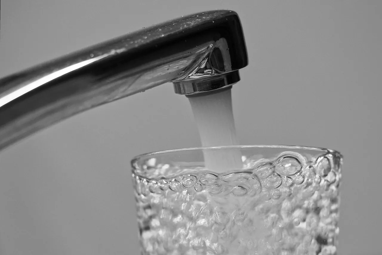 Agua saliendo de una canilla y llenando un vaso, el agua que pasa antes por el tanque domiciliario
